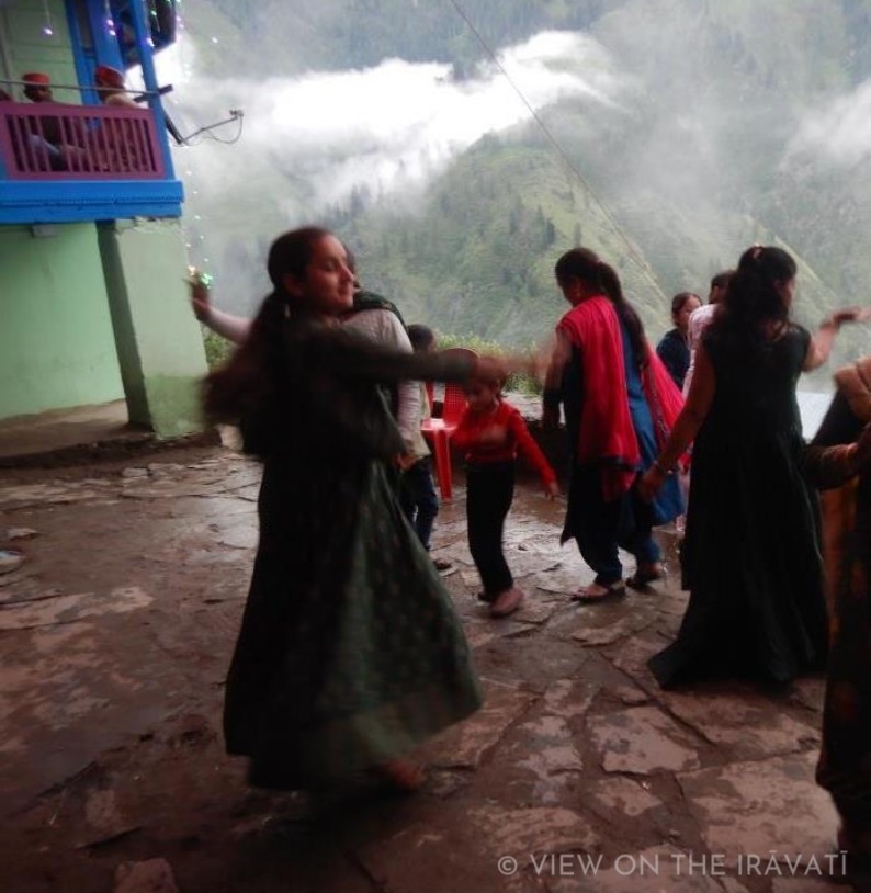 Gaddi women and children dancing at a marriage as clouds float by.
