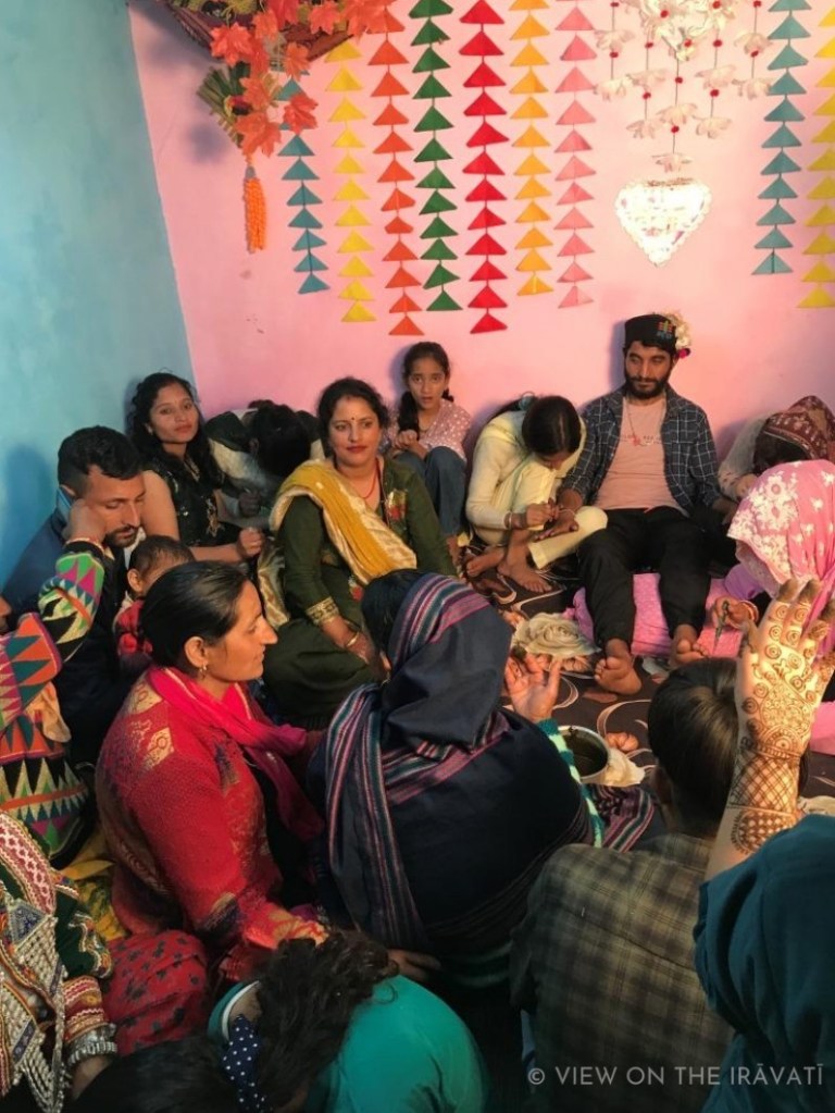 Gaddi family sit in brightly decorated room during Haldi ceremony.
